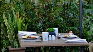 Una mesa al aire libre con platos de comida, una taza y una pequeña planta en maceta.