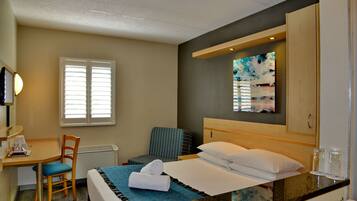 Quarto de hotel com cama, escrivaninha, cadeira, janela e um quadro na parede.