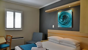 Una habitación de hotel con cama, escritorio, silla y un cuadro en la pared.