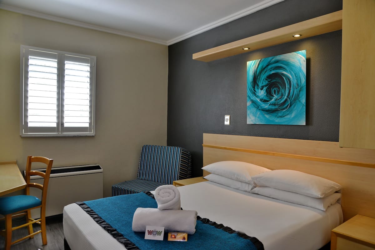 A hotel room with a bed, a desk, a chair, and a painting on the wall.