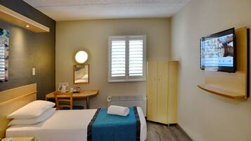 A hotel room with two beds, a desk, a chair, a TV, a mirror, and a window with blinds.