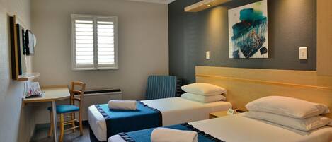 Habitación de hotel con dos camas individuales, un escritorio con silla, una ventana con persianas y un cuadro en la pared.