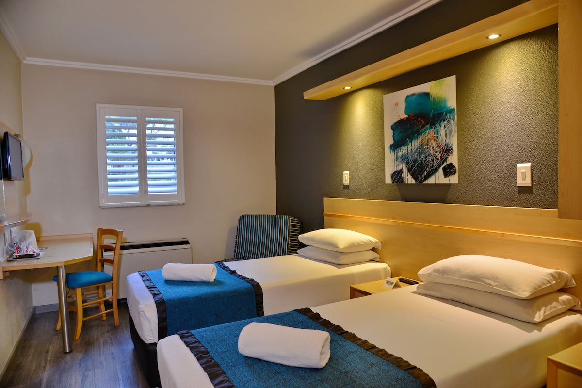 A hotel room with two beds, a desk, a chair, and a window with blinds.