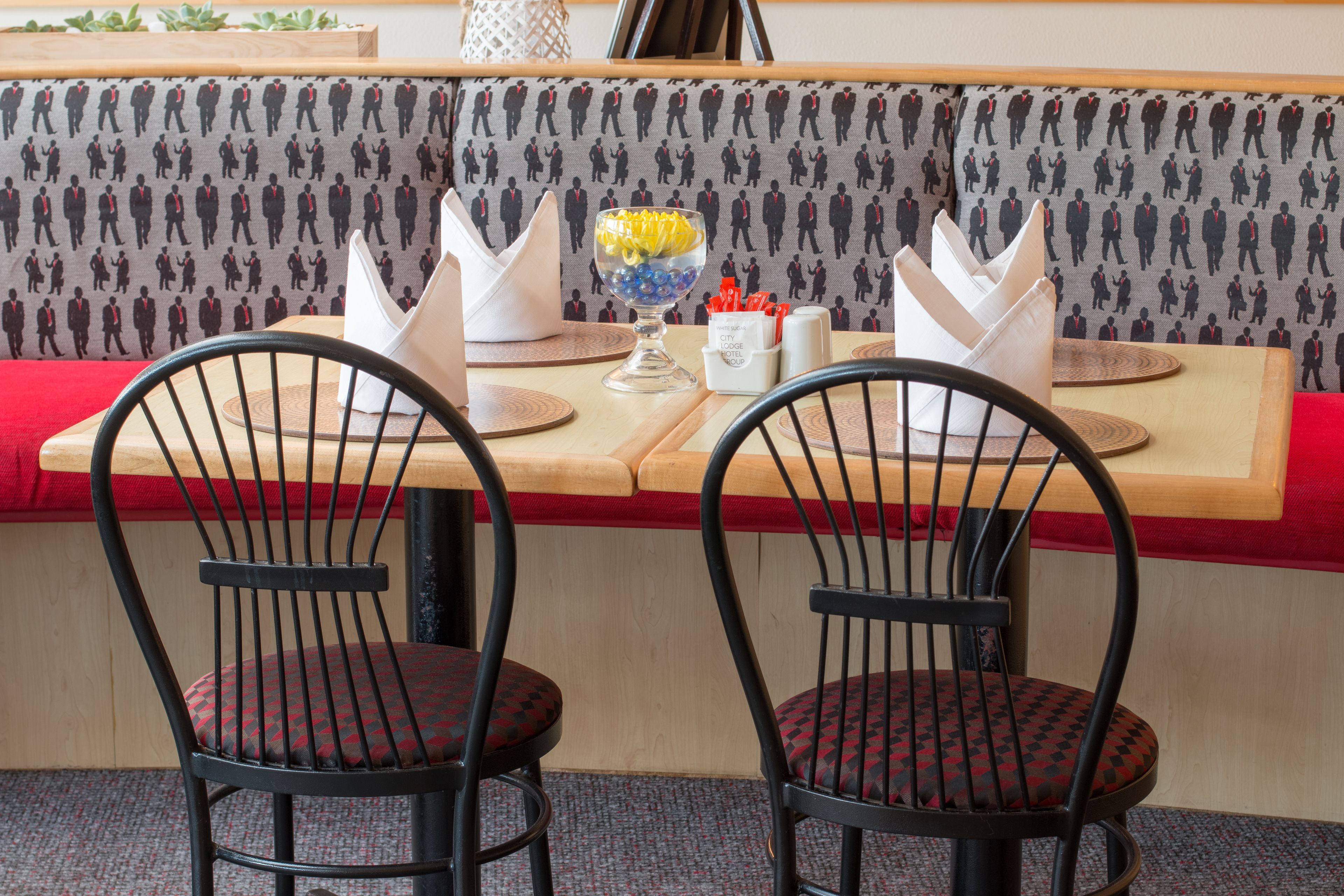 Eine Restaurantsitzgruppe mit gemustertem Wandpapier, einer Glasbowl mit gelben und blauen Gegenständen und einem Serviettenhalter.