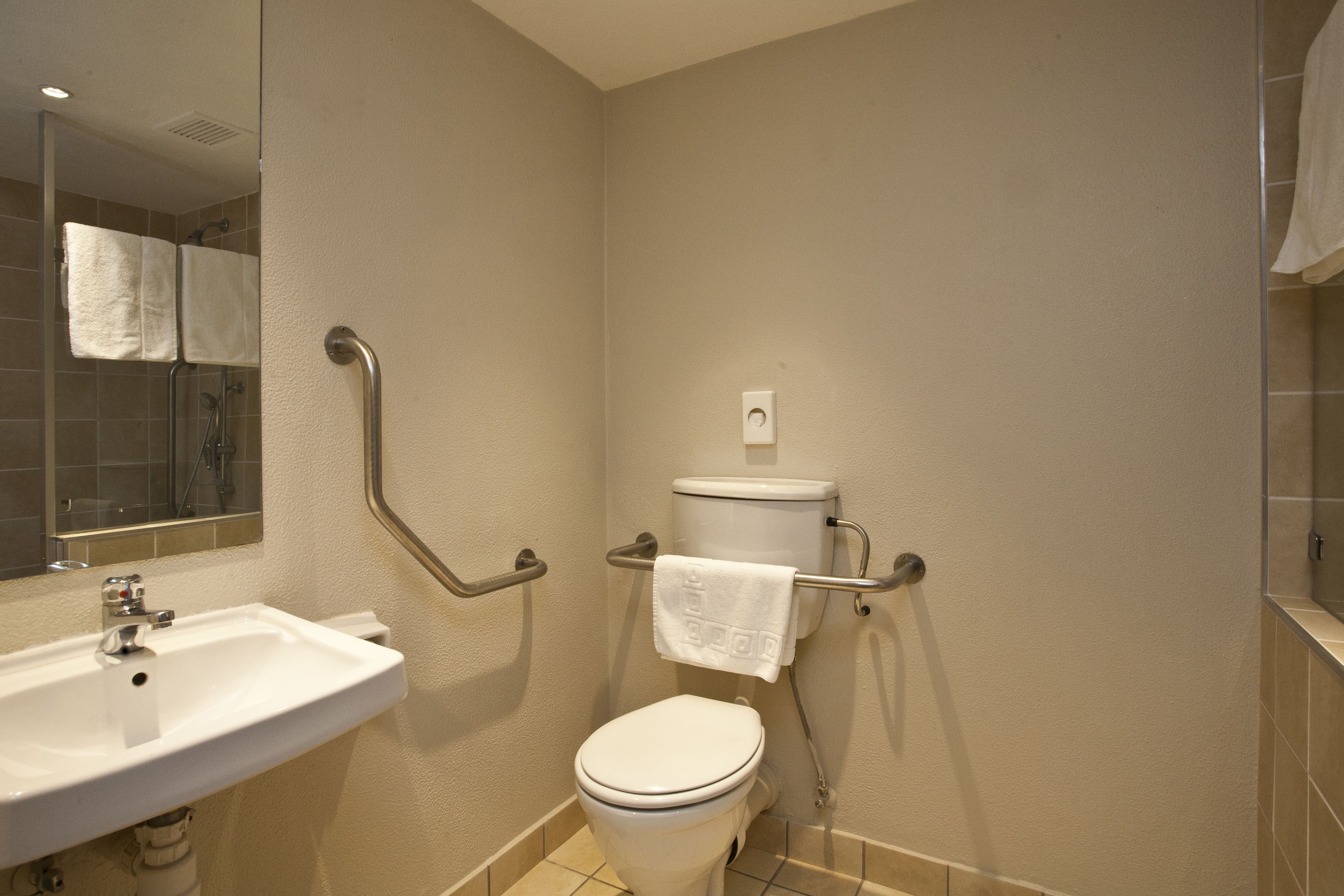 Un baño con lavamanos blanco, inodoro y barras de apoyo.