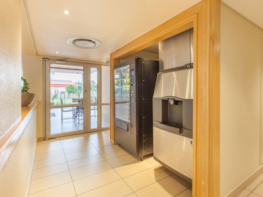 A hotel corridor with a refrigerator, a plant, and a sliding glass door leading to an outdoor area.