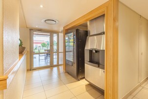 Pasillo de hotel con refrigerador, una planta y puerta corrediza de vidrio que da a un área exterior.
