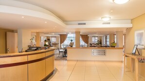 Un espace d’accueil d’hôtel avec un comptoir d’accueil incurvé, un coin salon avec des chaises et un panneau indiquant les numéros de chambre et les indications.