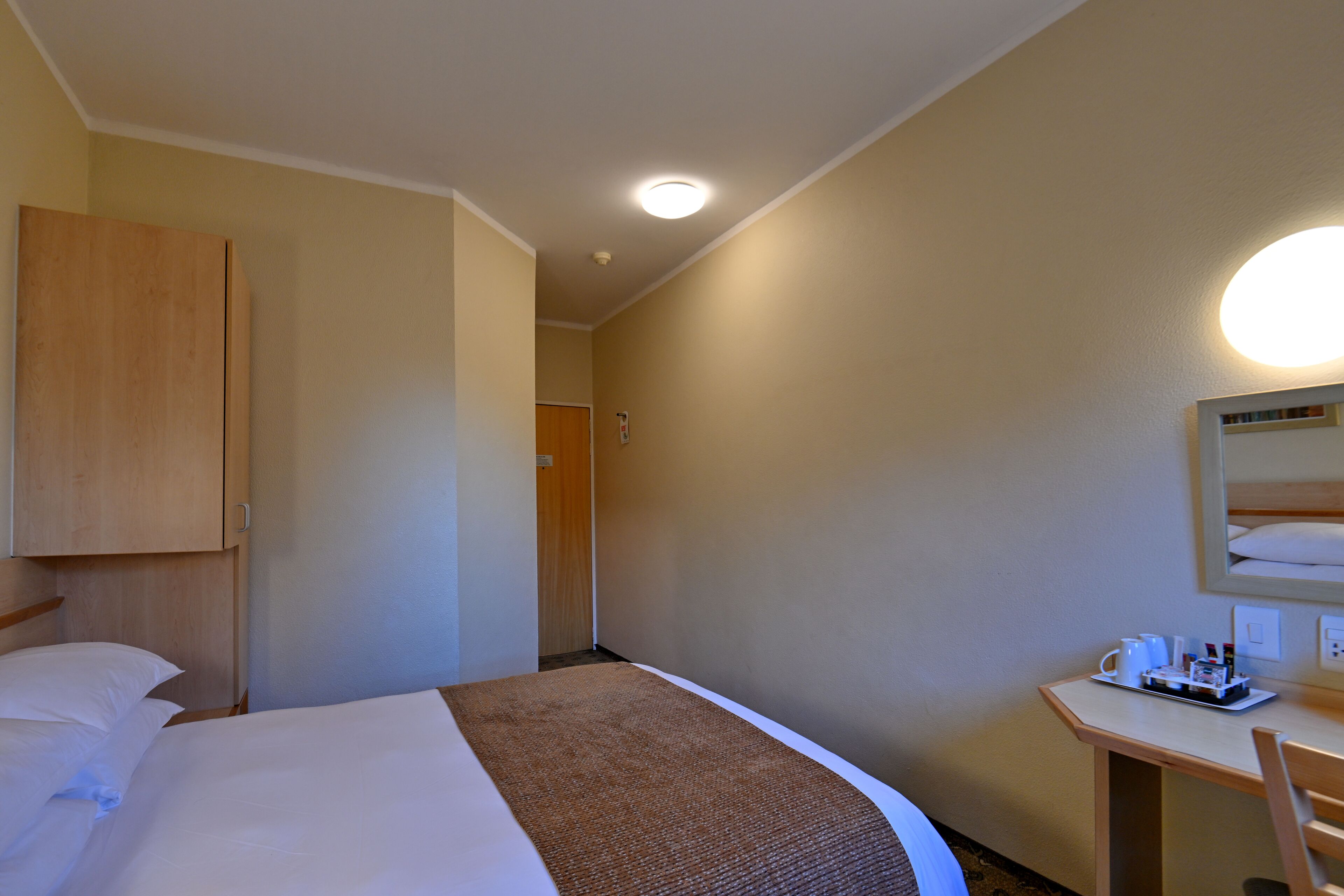 A hotel room with a bed, a desk, and a mirror.