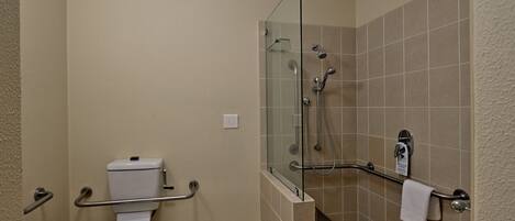 A bathroom with a toilet, a glass shower enclosure, and a grab bar.