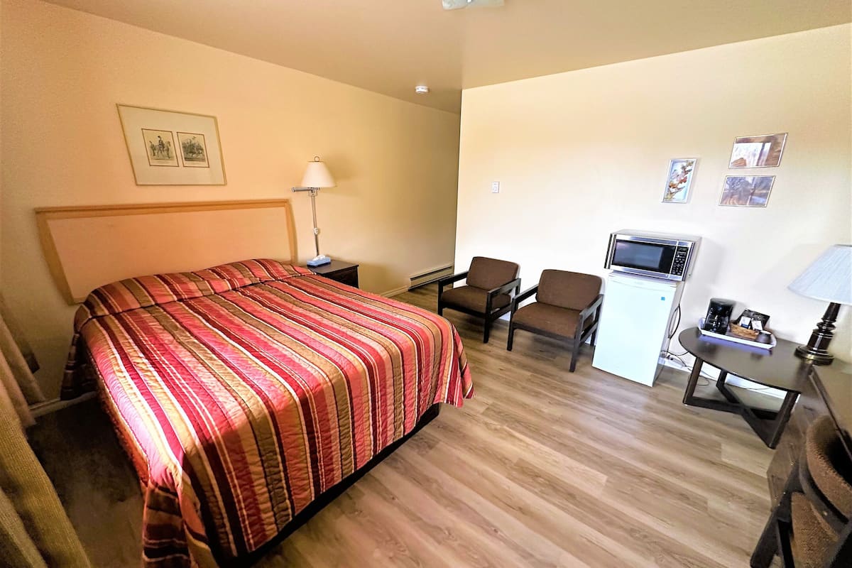 A hotel room with a bed, two armchairs, a small desk with a microwave, and a lamp.