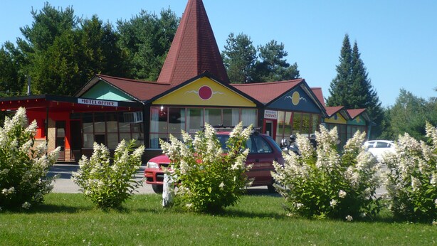 Et motel med et markant rødt tag og en gul facade, inklusive en restaurantindgang og et synligt parkeringsområde.