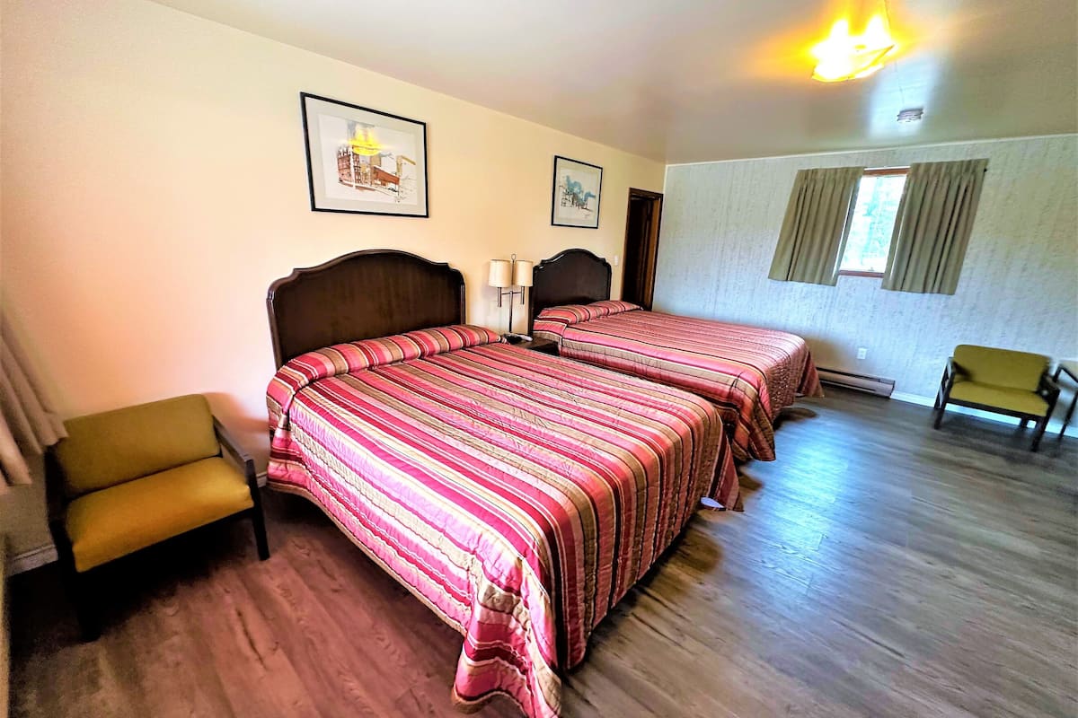 A bedroom with two beds, a chair, a sofa, and a window with curtains.