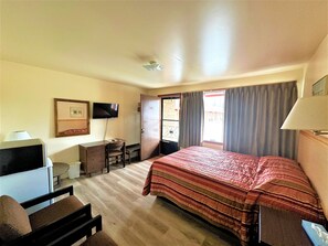 A hotel room with a bed, a desk, a chair, a television, and a window with curtains.