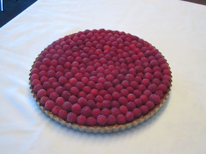 A round tart with a raspberry topping, placed on a white tablecloth.
