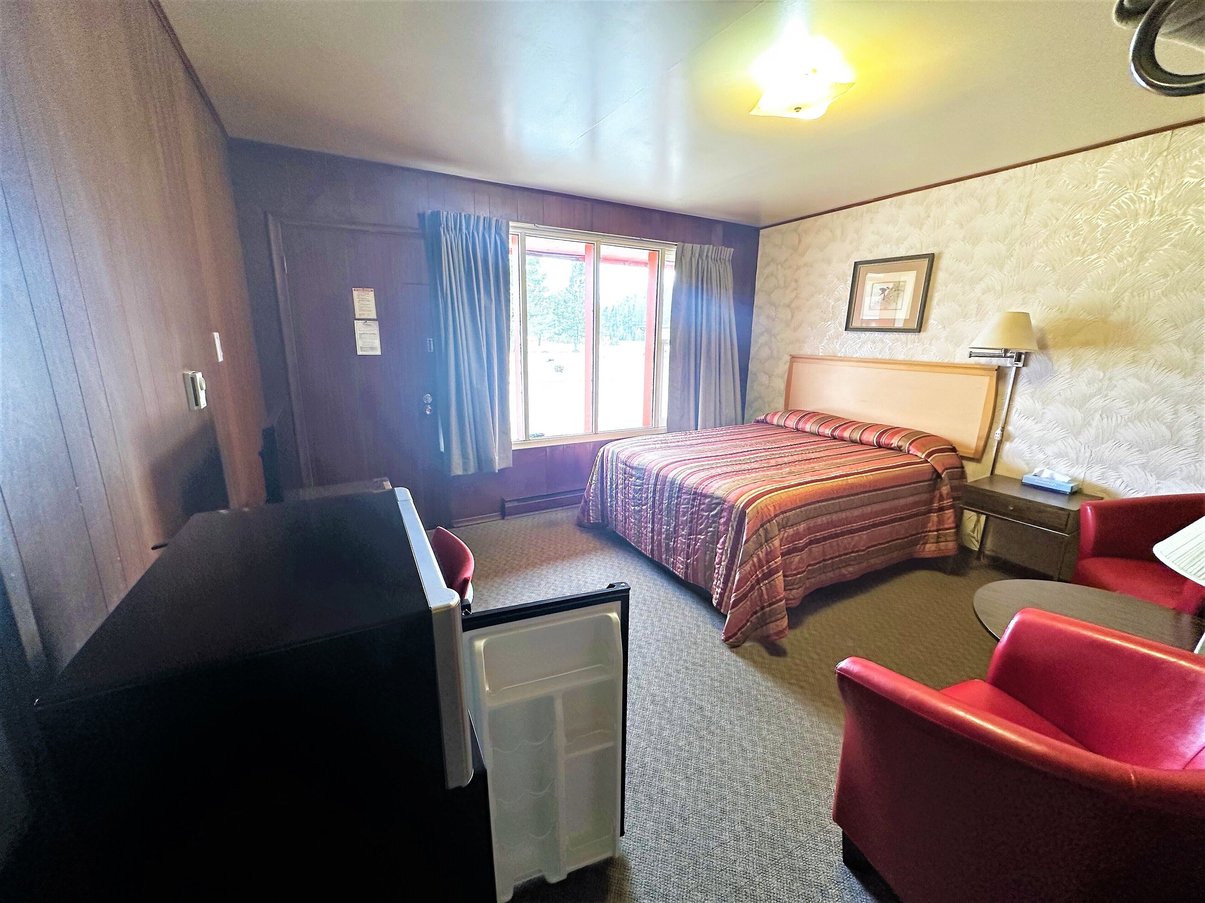 A hotel room with a bed, a desk, a chair, a lamp, and a window with curtains.