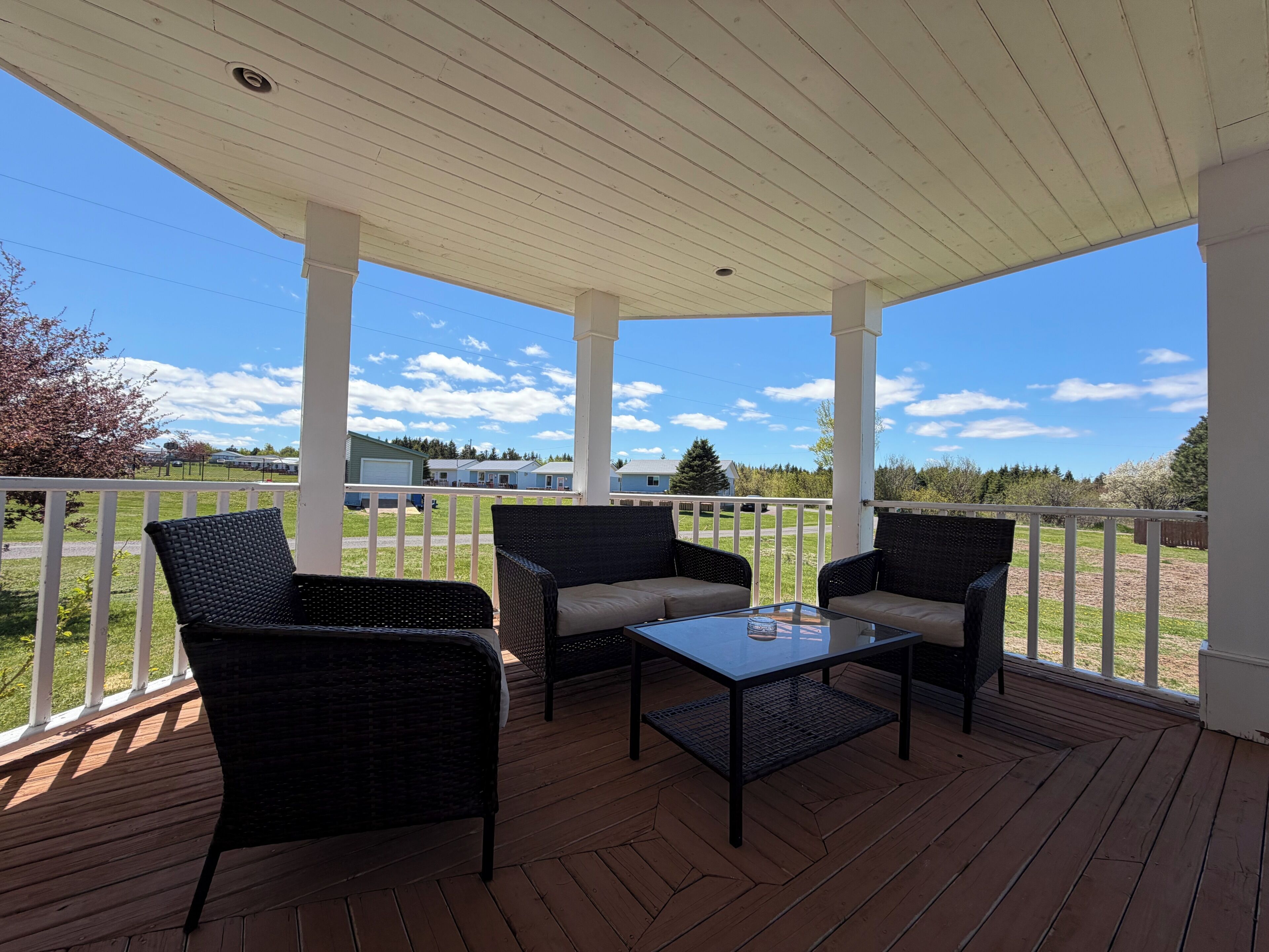 A covered outdoor area with wicker furniture and a glass table, overlooking a residential area.