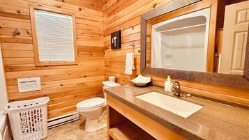 Un baño con paneles de madera, un lavamanos, un espejo, un inodoro y un cartel para toallas usadas.