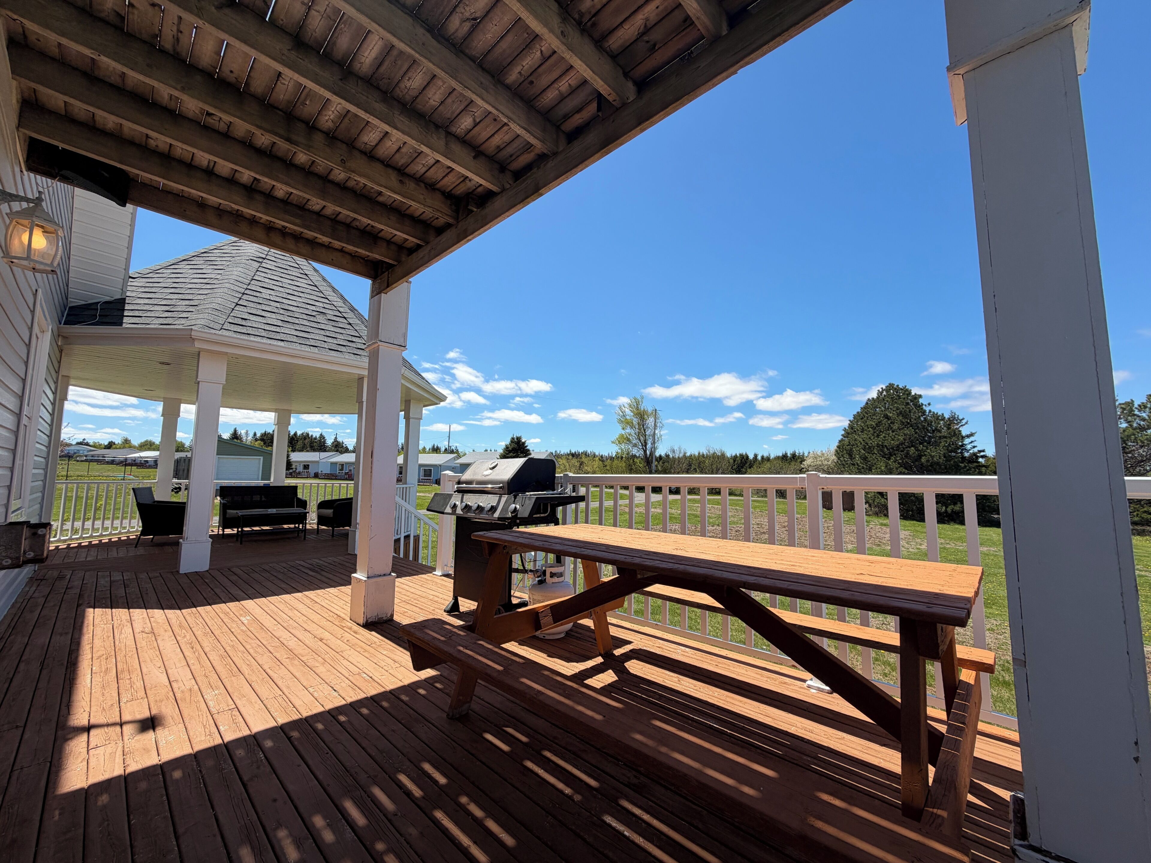 Un espacio al aire libre techado con una terraza de madera, un quiosco y una parrilla de barbacoa.