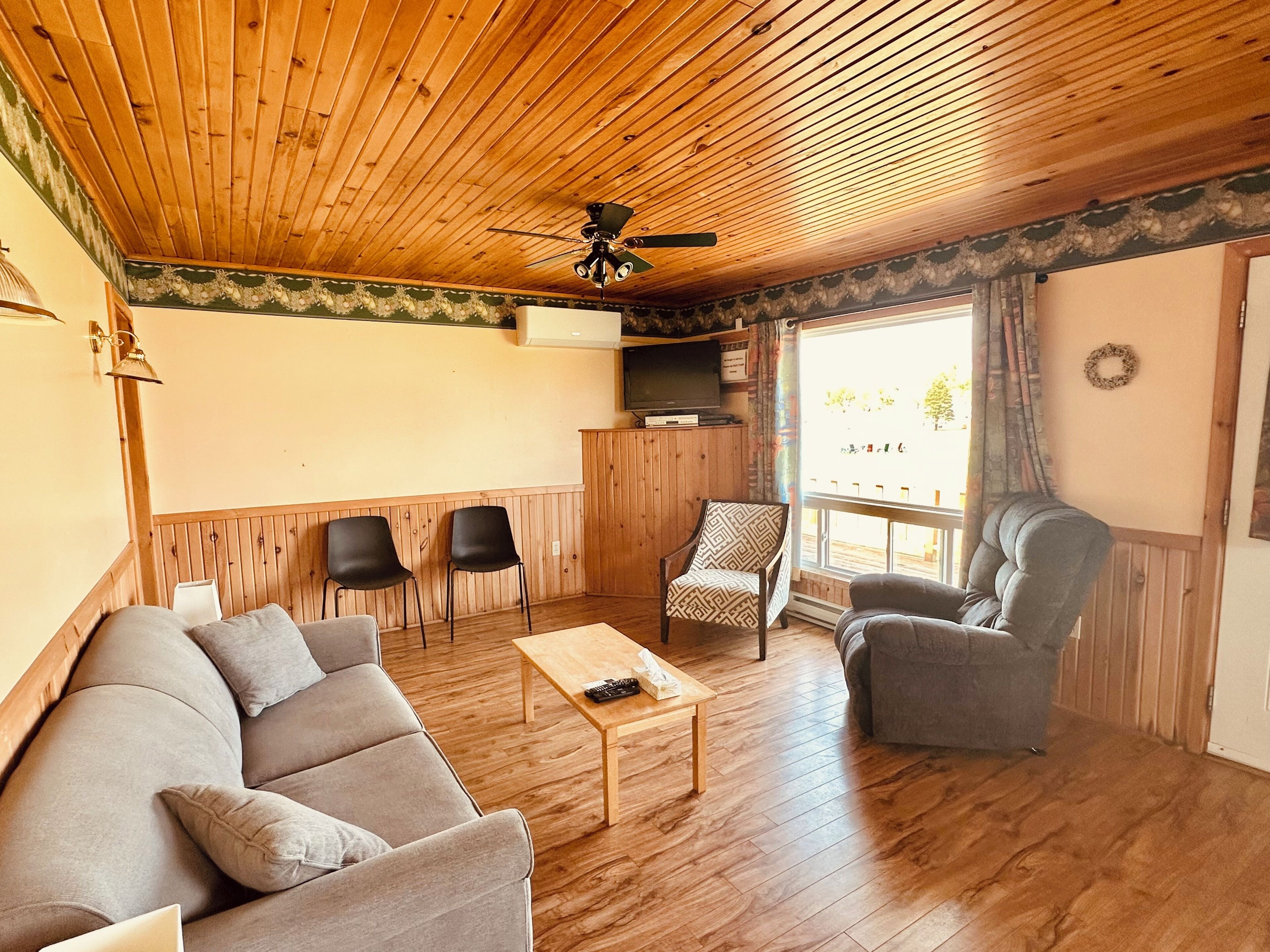 A wooden-paneled room with a sofa, two chairs, a coffee table, and a ceiling fan.