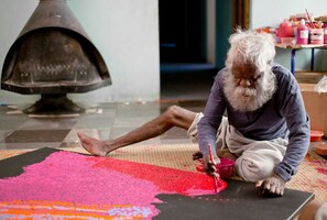 Una persona sentada en el suelo, pintando sobre una superficie amplia con una paleta de colores.