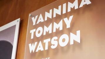 Un letrero con el texto 'YANNIMA TOMMY WATSON THE ARTIST' en una pared de madera.
