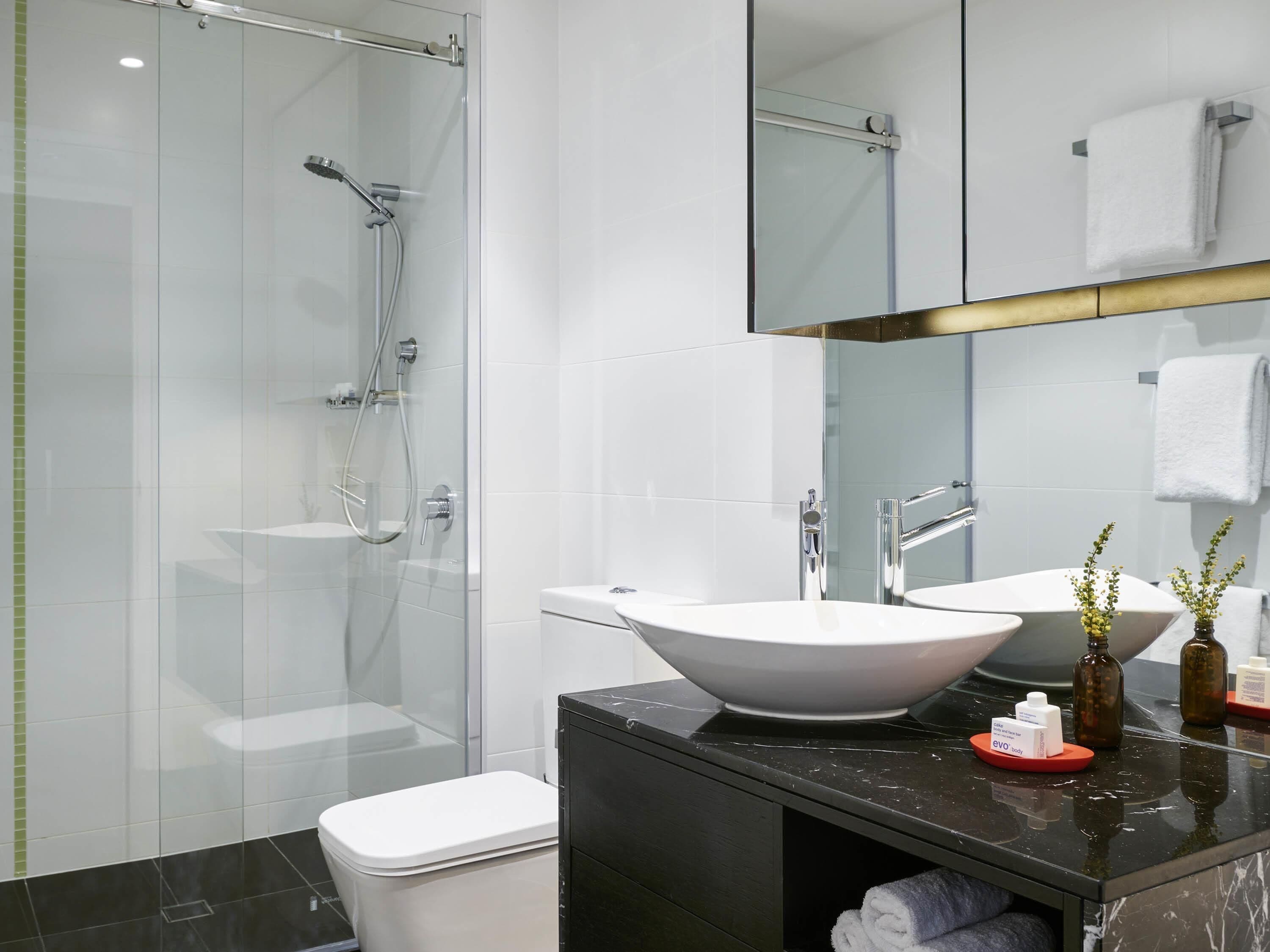 A modern bathroom with a glass-enclosed shower, a white vessel sink, and a dark marble countertop.