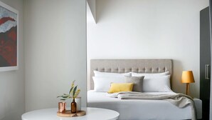 A modern bedroom with a bed, bedside lamp, and a round table with chairs. - Art Series - The Watson (Walkerville)