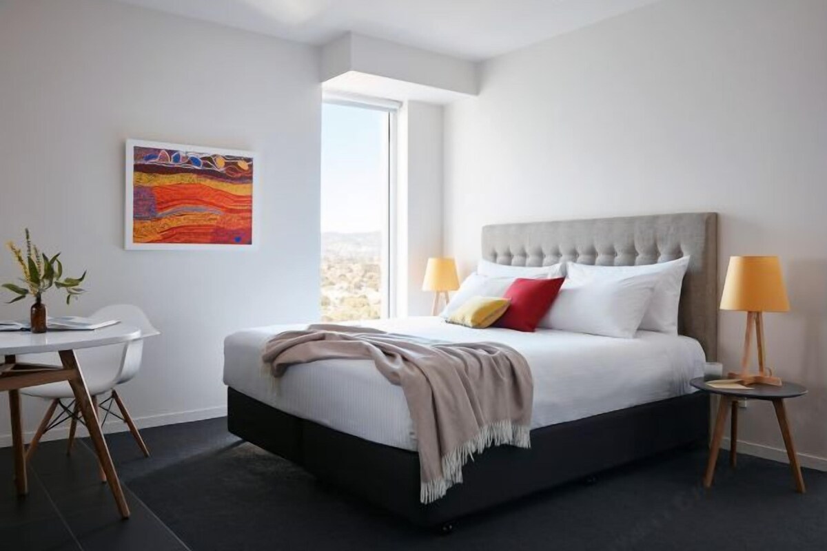 A modern bedroom with a large bed, bedside lamps, a desk, and a window with a view.
