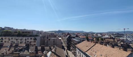 A cityscape with a mix of historic and modern buildings, a clear sky, and distant hills.