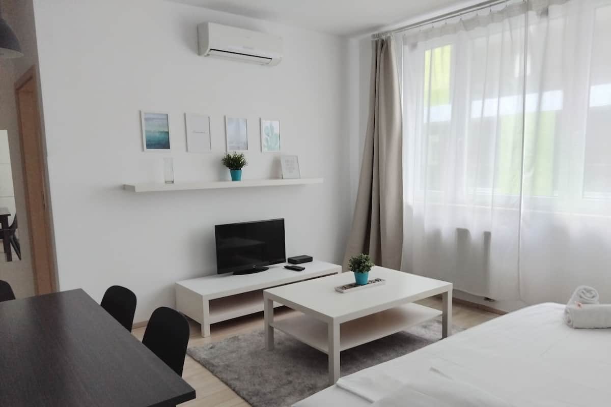A modern hotel room with a bed, a desk, a TV, and a small coffee table.