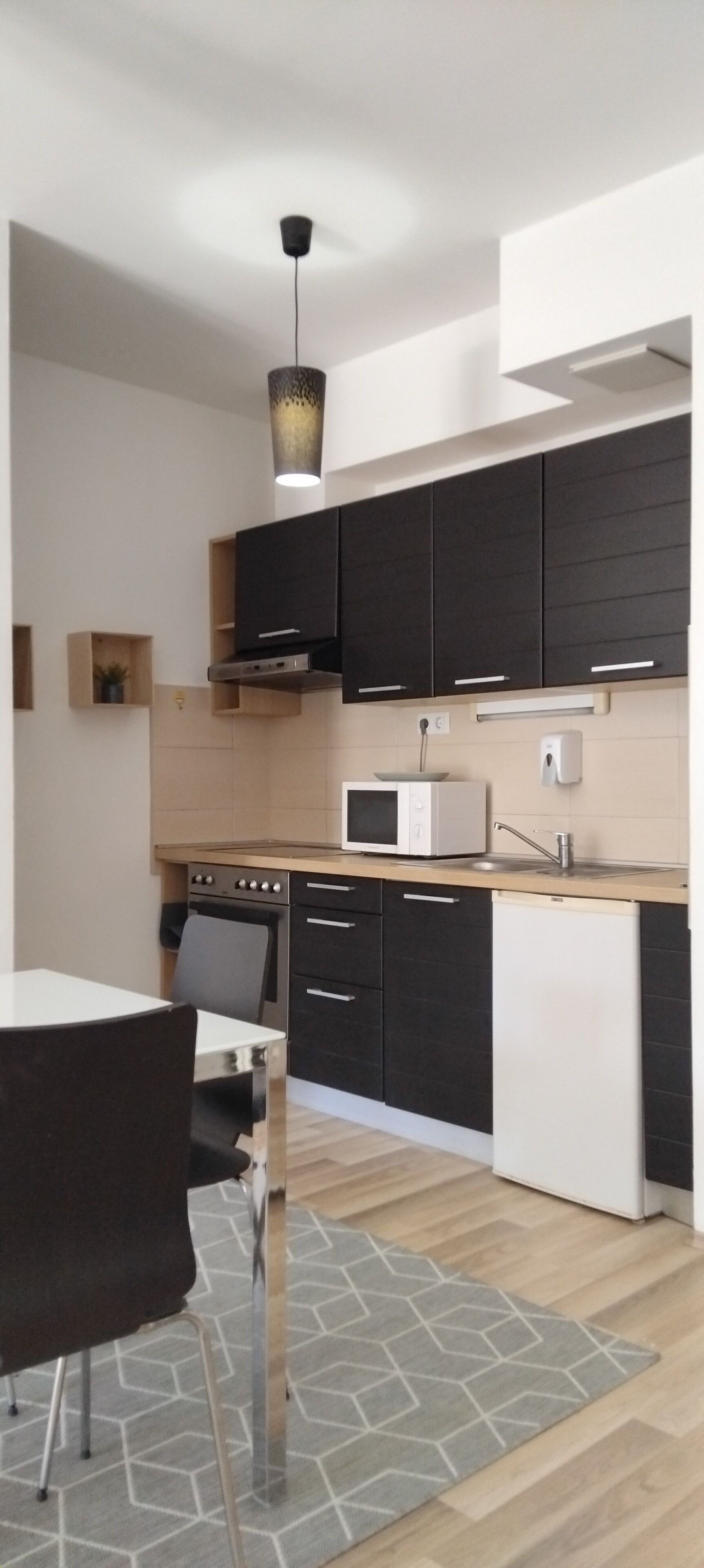 Una cocina moderna con armarios negros, un microondas blanco y una campana extractora de acero inoxidable.