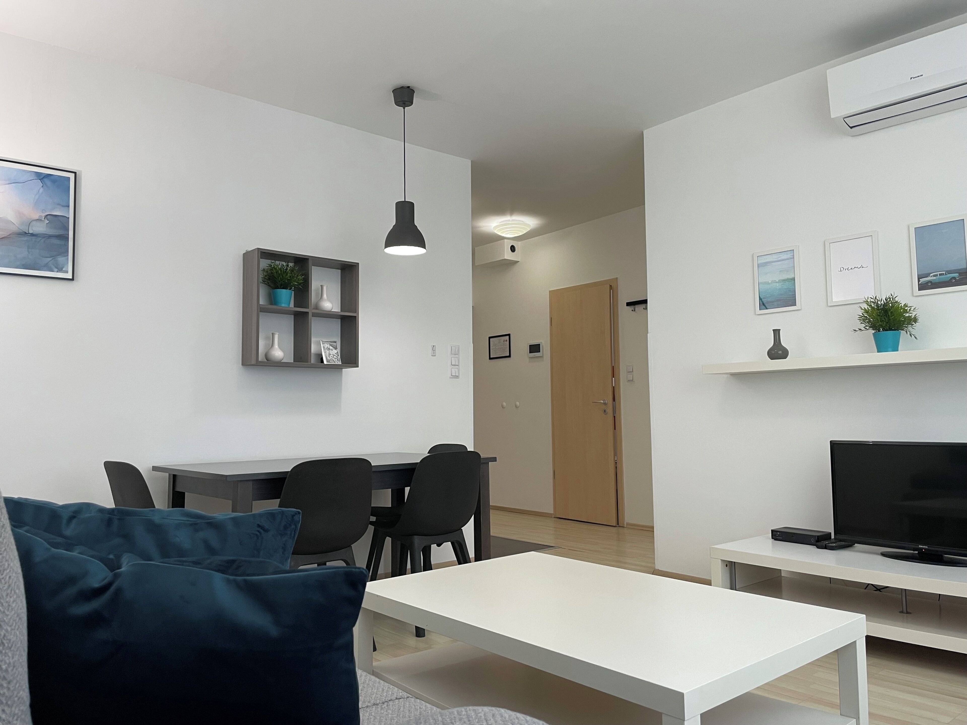 Una sala moderna con un sofá blanco, una mesa de comedor con sillas, un mueble para TV y un estante empotrado con adornos.