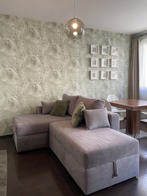 A modern living room with a sectional sofa, a dining table, and a wall with framed pictures. - Corvin Center Suites (Budapest)