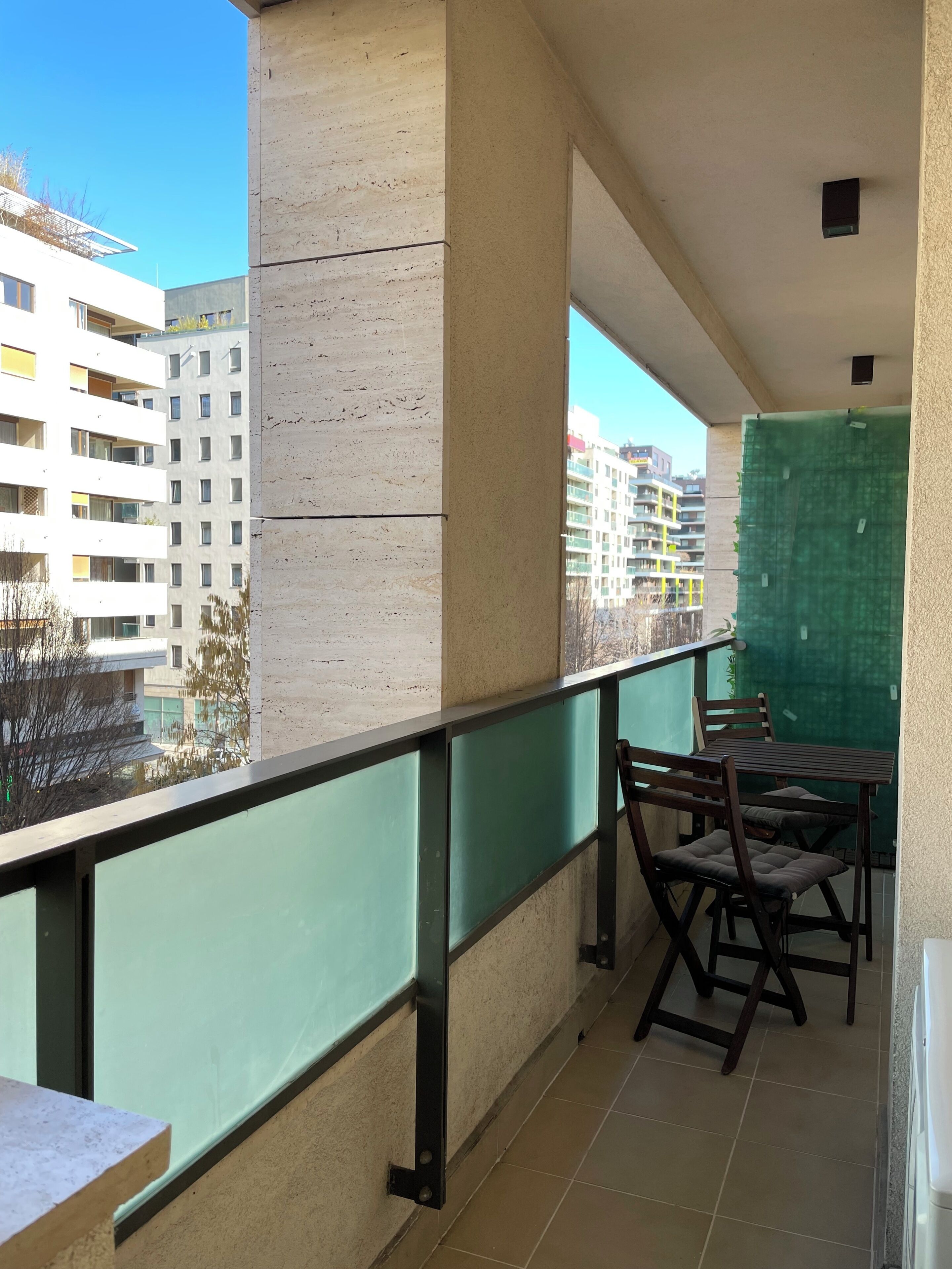 A balcony with a table and chairs, a green screen, and a view of buildings.