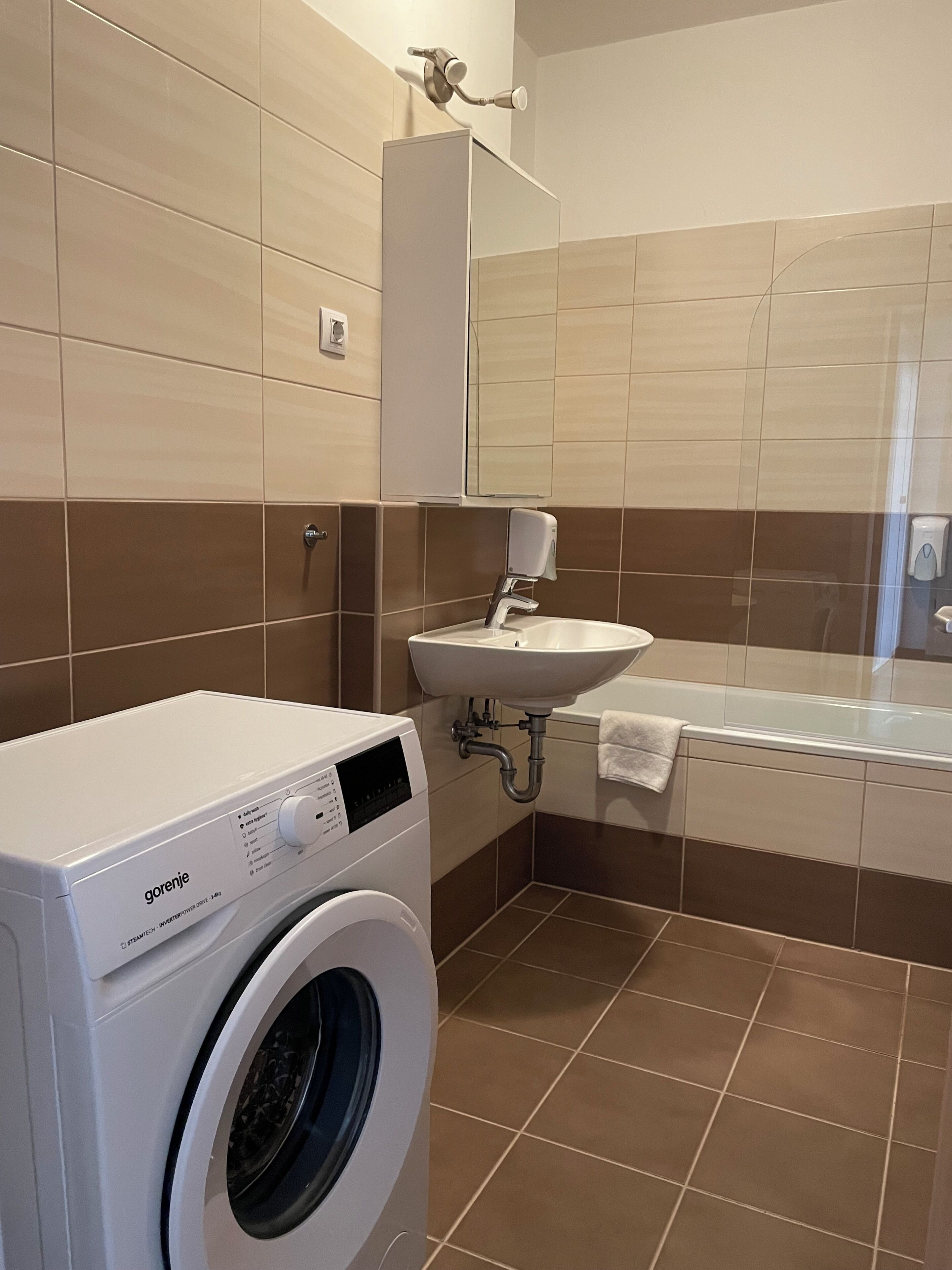 A modern bathroom with a washing machine, sink, and bathtub.