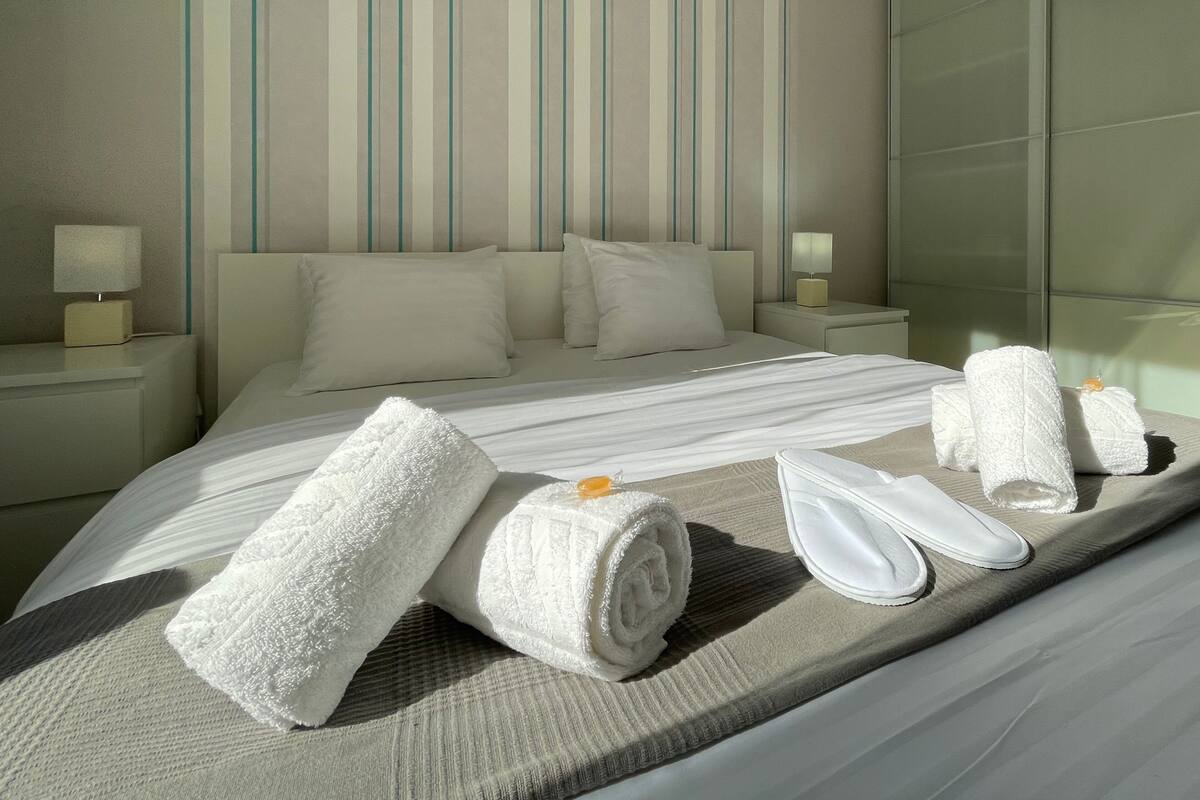 A hotel room with a large bed, two bedside tables, a mirror, and towels.