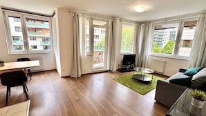 Un appartement moderne comprenant un coin repas, un salon avec un canapé et un téléviseur, ainsi que de grandes fenêtres offrant une vue sur la ville.