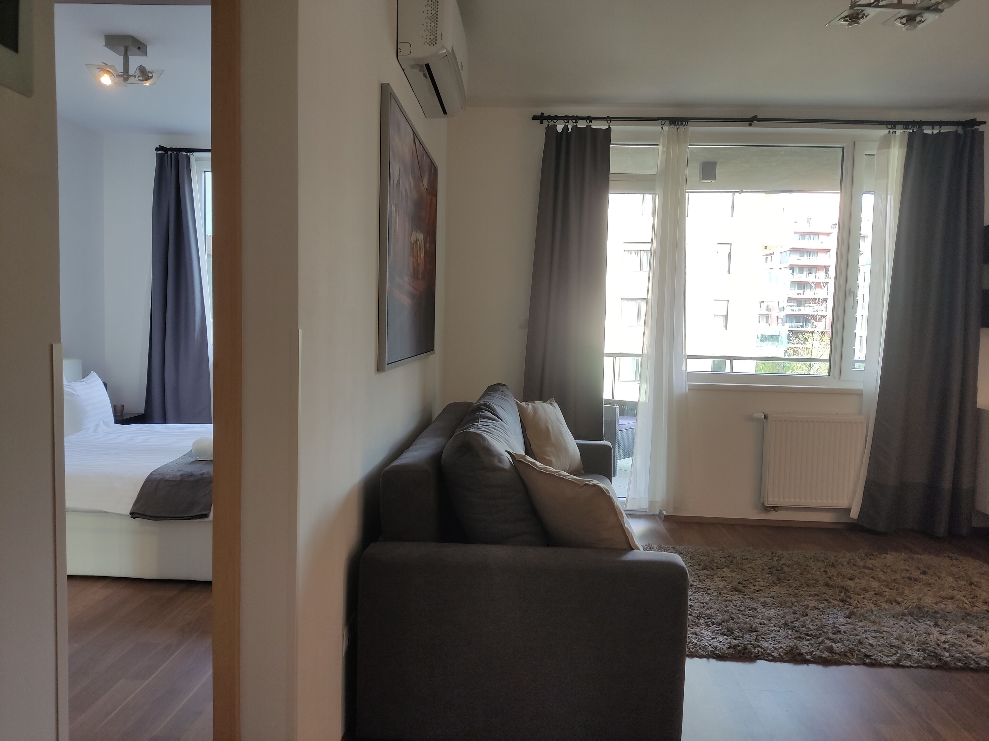 A modern living room with a sofa, a bed, and a large window with curtains.