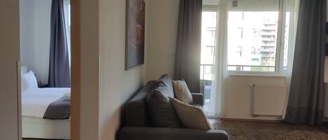 A modern living room with a sofa, a bed, and a large window with curtains.