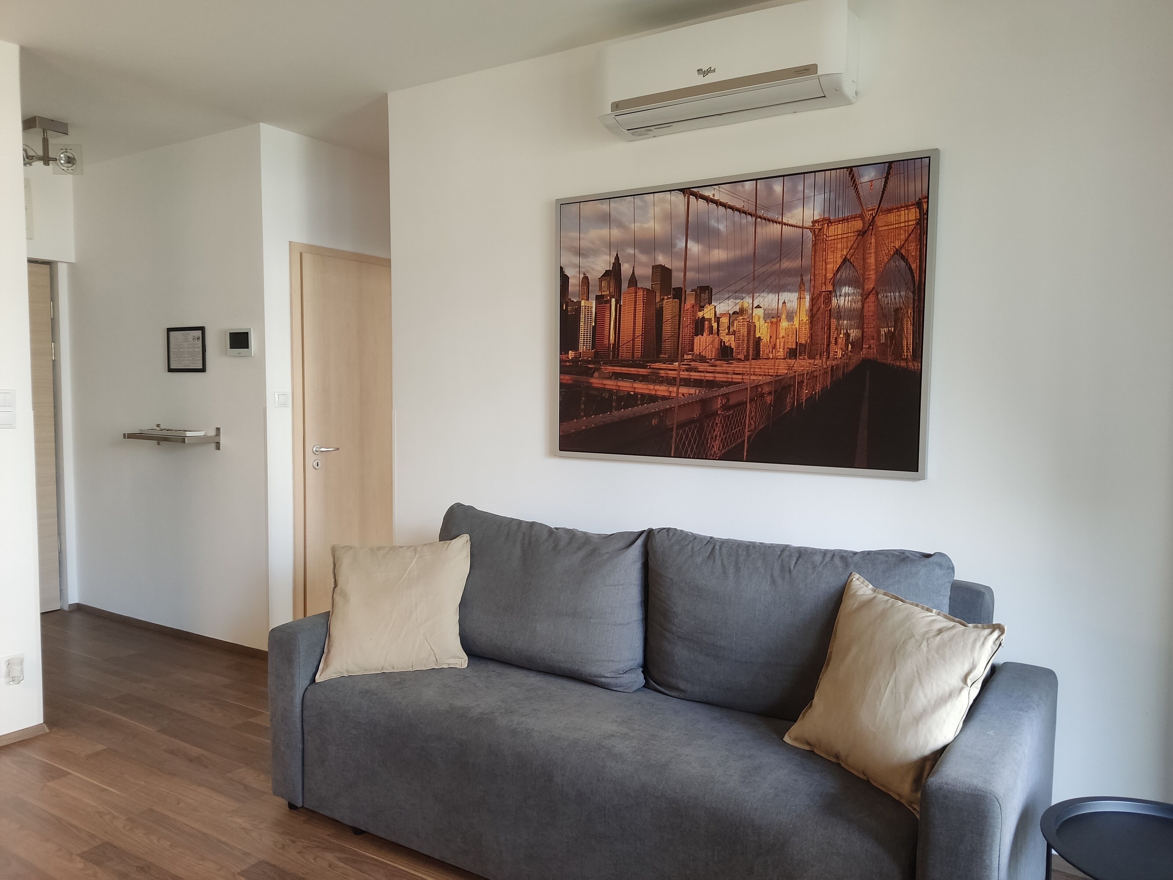 A modern living room with a grey sofa, a cityscape painting, and a wooden floor.