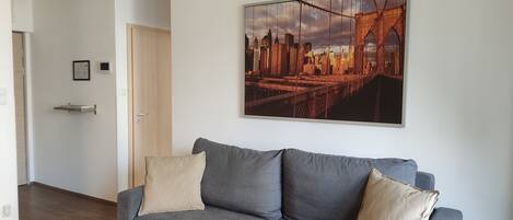 Una sala moderna con un sofá gris, un cuadro de un paisaje urbano y suelo de madera.