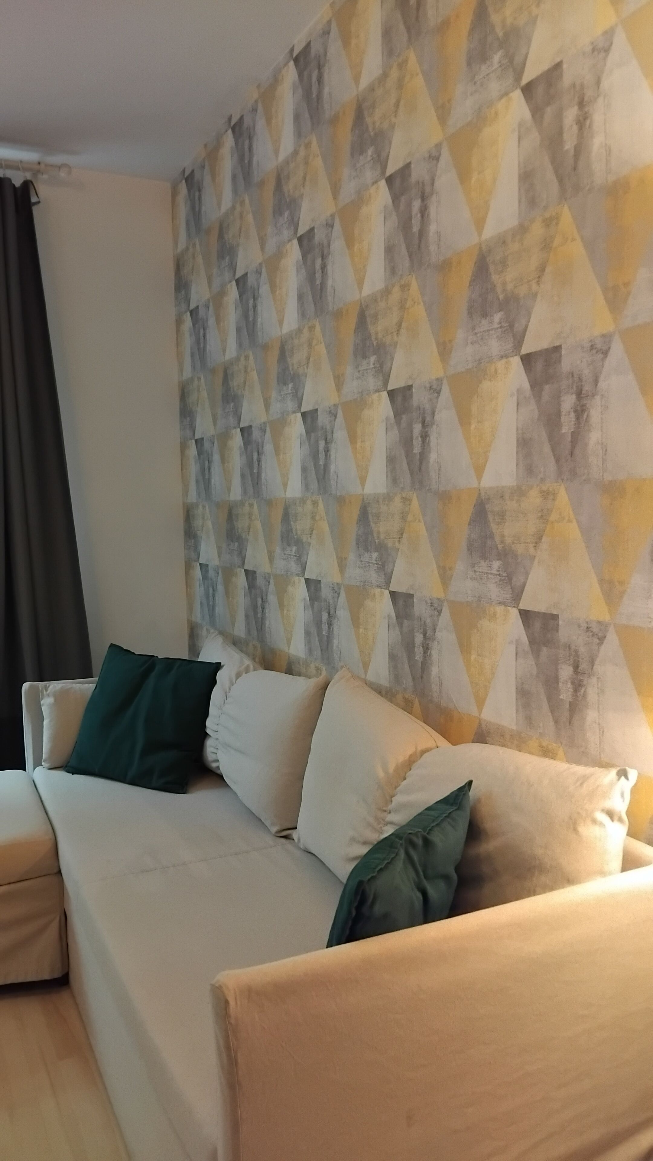 A living room with a sofa and pillows, a patterned wall, and a window with curtains.