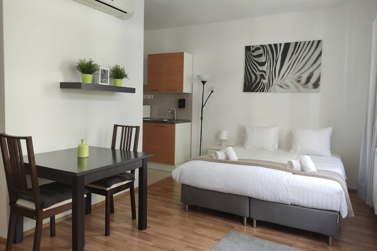 A modern bedroom with a bed, bedside table, and a small kitchen area.