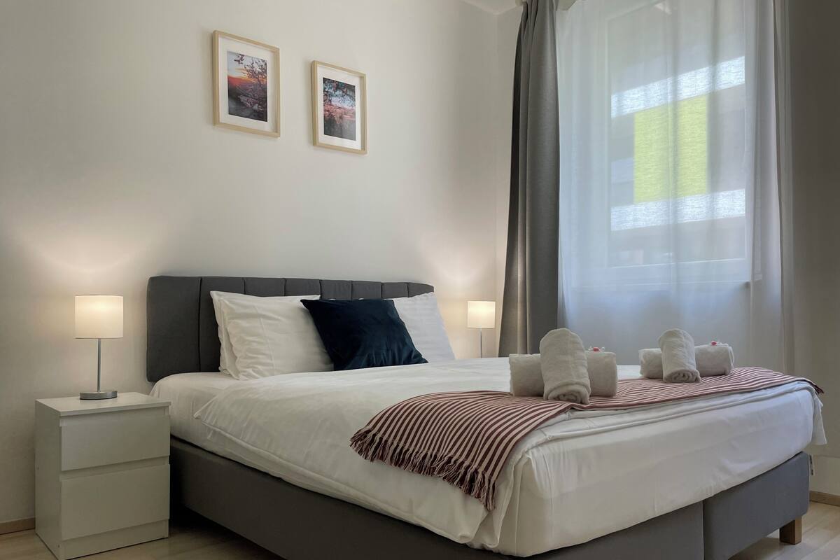 A modern bedroom with a bed, bedside lamps, a nightstand, and two framed pictures on the wall.