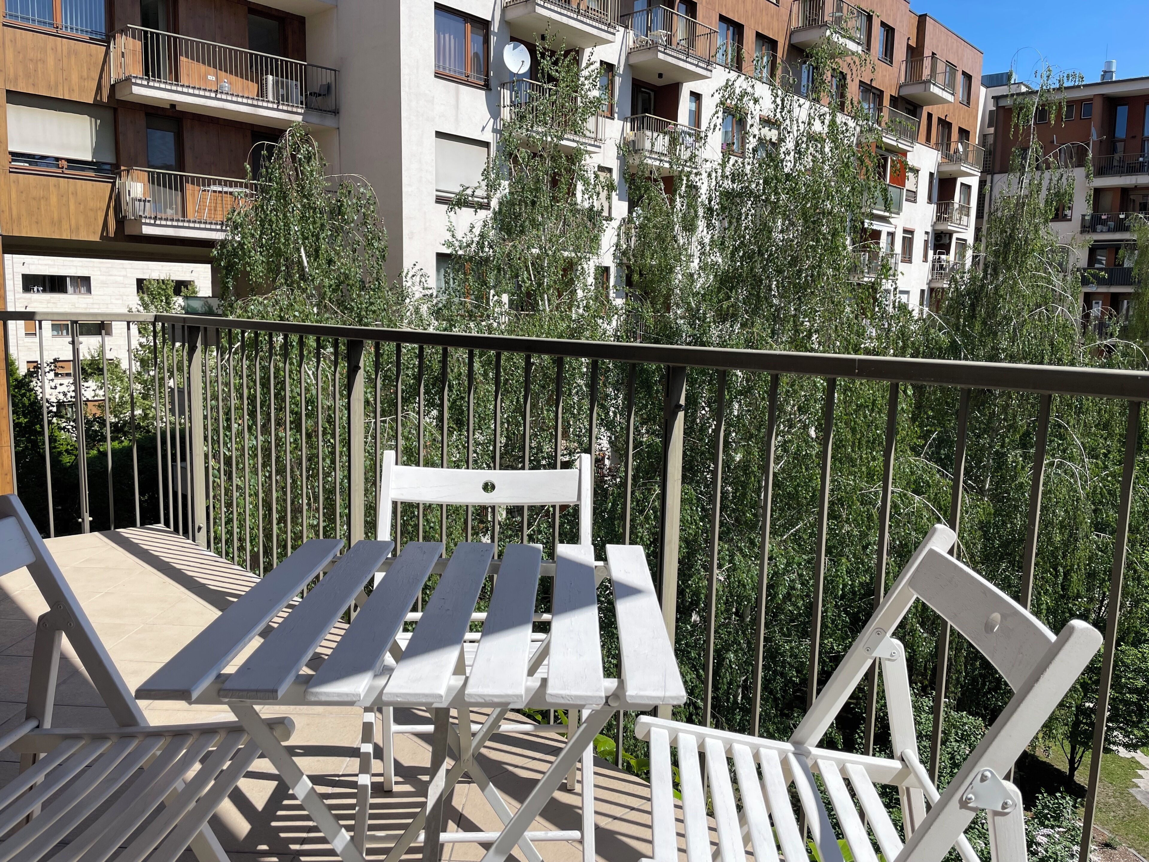 A balcony with white metal railings, a white table, and a white chair.