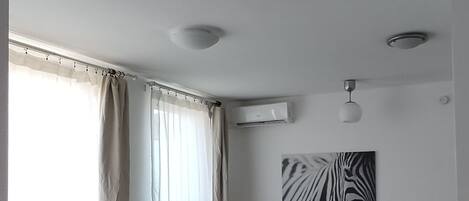 Una sala de estar moderna con un sofá gris, una pequeña mesa redonda de madera con una planta, un tapete verde y un cuadro de pared con estampado de cebra.