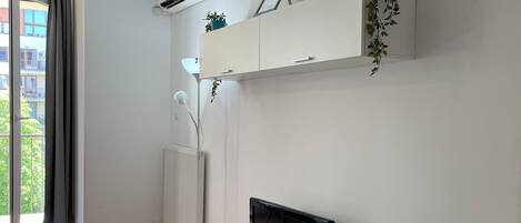 Una sala de estar moderna con un televisor de pantalla plana sobre una consola blanca, un radiador y una planta en maceta en un estante.