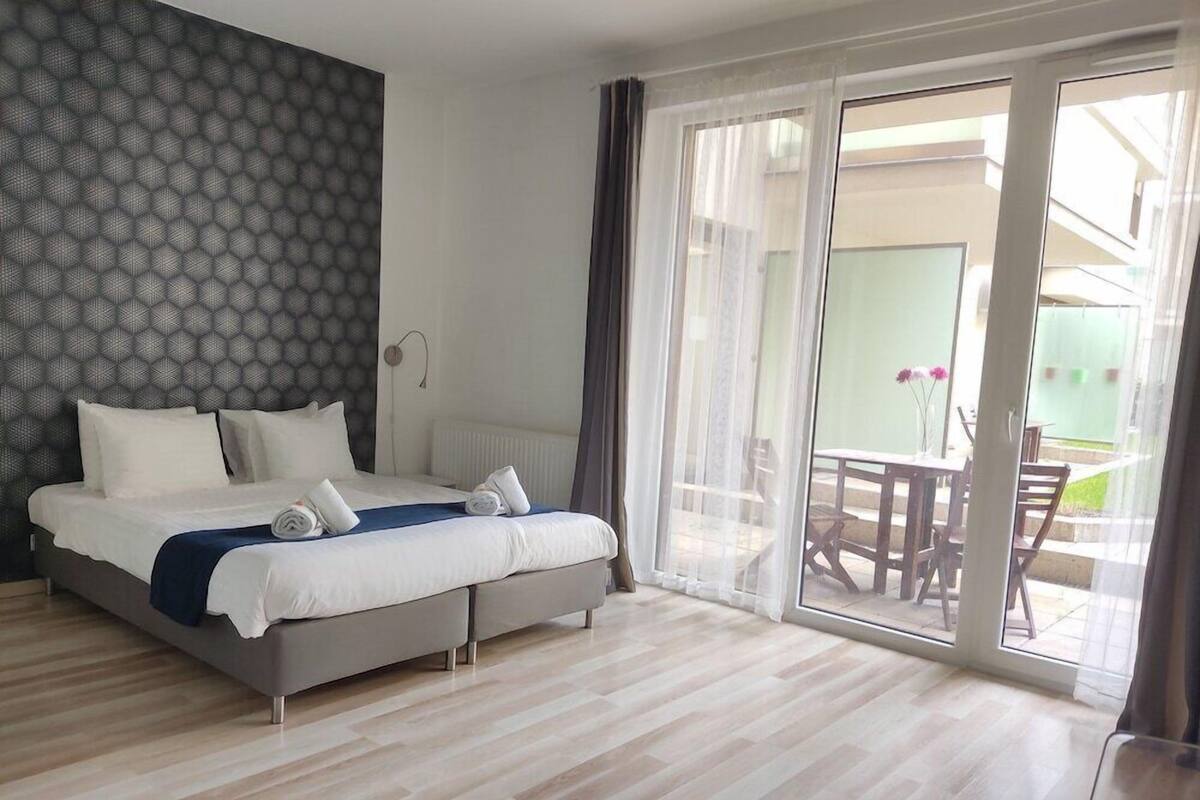 A modern hotel room with a large bed, a view of the outdoor patio, and a patterned wall.