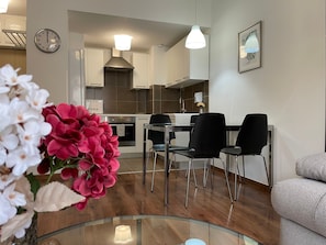 A modern kitchen with white cabinets, a stainless steel range hood, and a dining area with black chairs and a glass table. - Corvin Center Suites (Budapest)